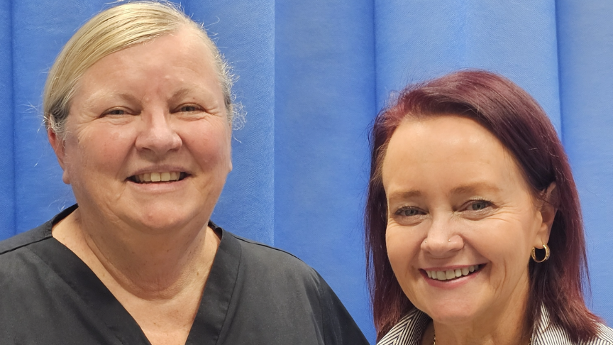 Headshot of two nurses standing in front of a blue curtain