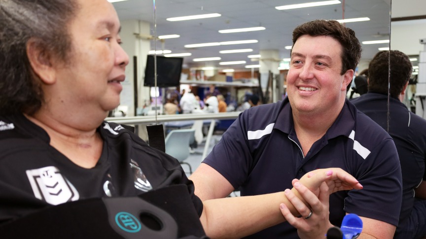 Physiotherapist Jai Peach assists a patient in a gym setting, both engaged in conversation
