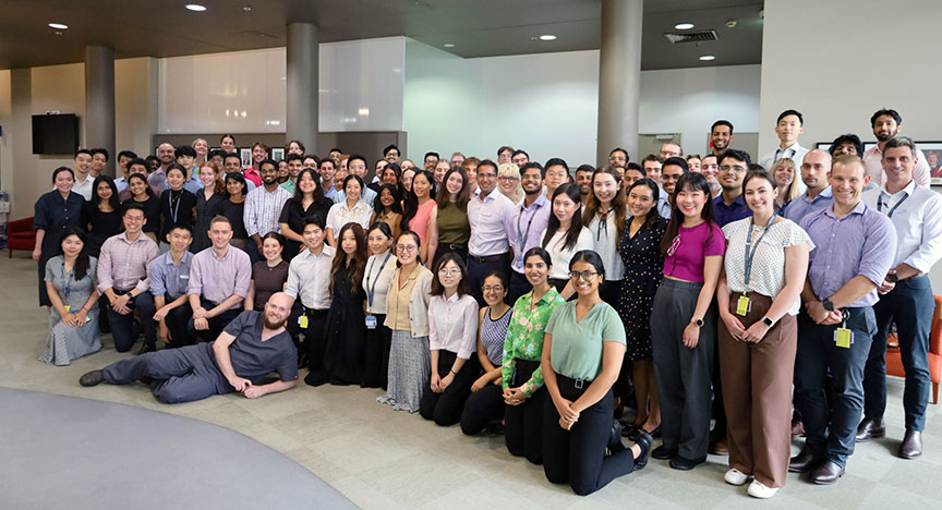 A large group of medical interns and staff pose together in a hospital setting, smiling and standing closely.