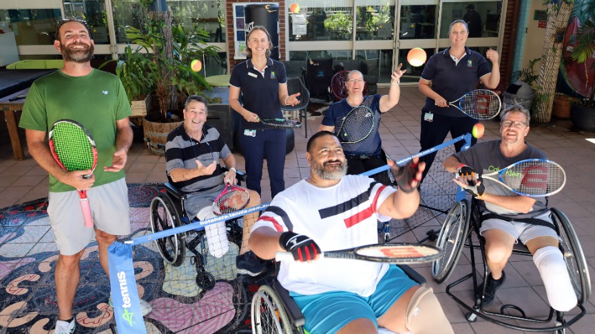 A group of individuals in wheelchairs, each holding tennis rackets, participating in a wheelchair tennis program at Bunya Ward