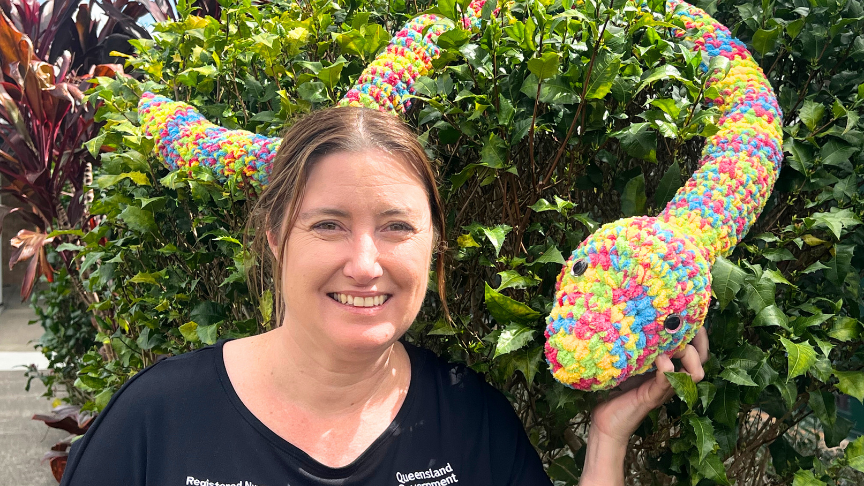 Nurse in navy scrubs holding a giant crocheted python
