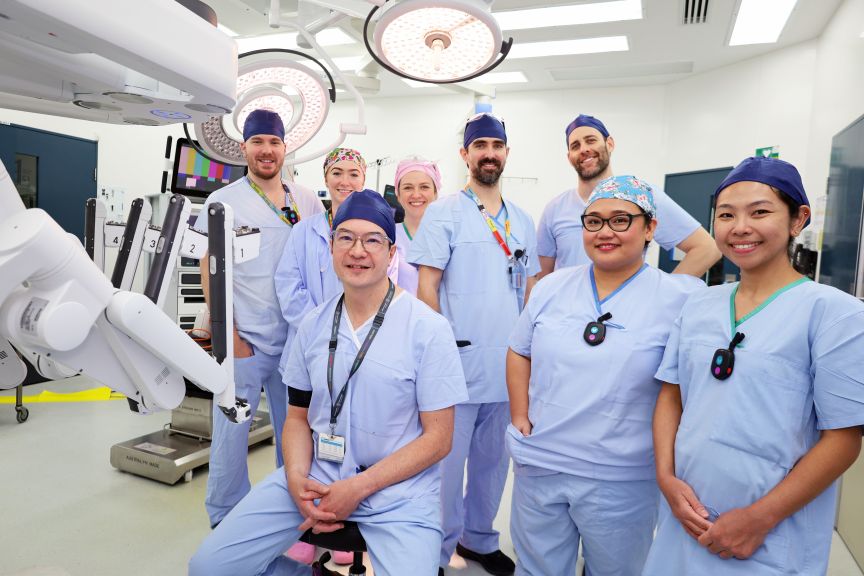 A team of surgeons, anaesthetists and nurses in a theatre wearing scrubs with a surgical robot