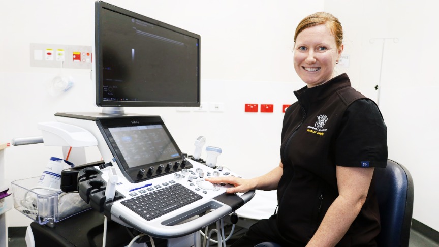 Female Sonographer sitting in front of sonography computer and smiling.