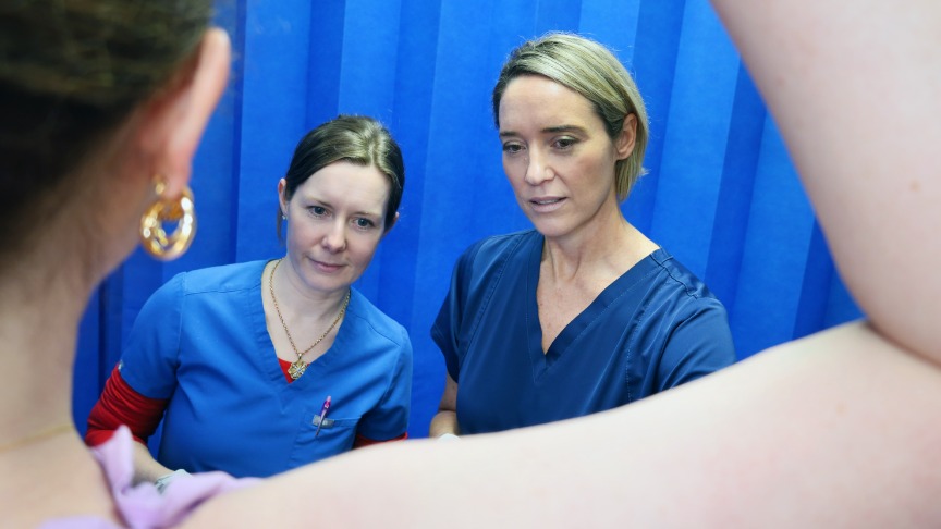 Backwards view of two female dermatologists looking at female patient armpit