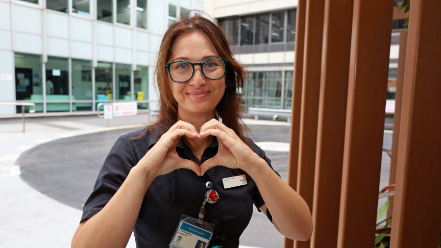 A female nurse educator pictured outside a hospital holding her hands in a heart shape
