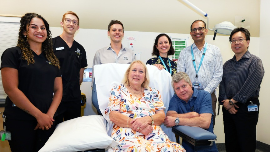 A group of healthcare professionals surrounds cancer patient Pam in a hospital room, offering support and care