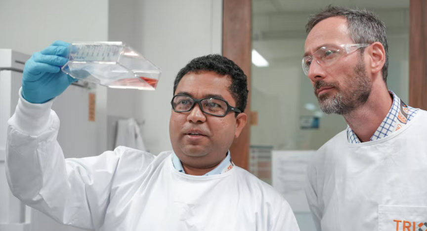 Two researchers in lab coats examine a container with a liquid sample in a laboratory setting.