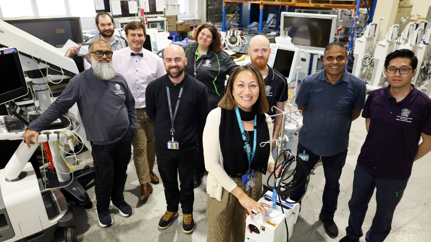A group of people, including Kijiana, stands in front of a machine, representing the asset team