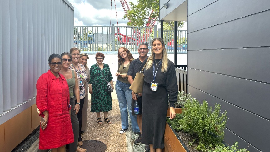 A group of mental health staff members standing in front of a crisis support building, smiling and engaged in conversation