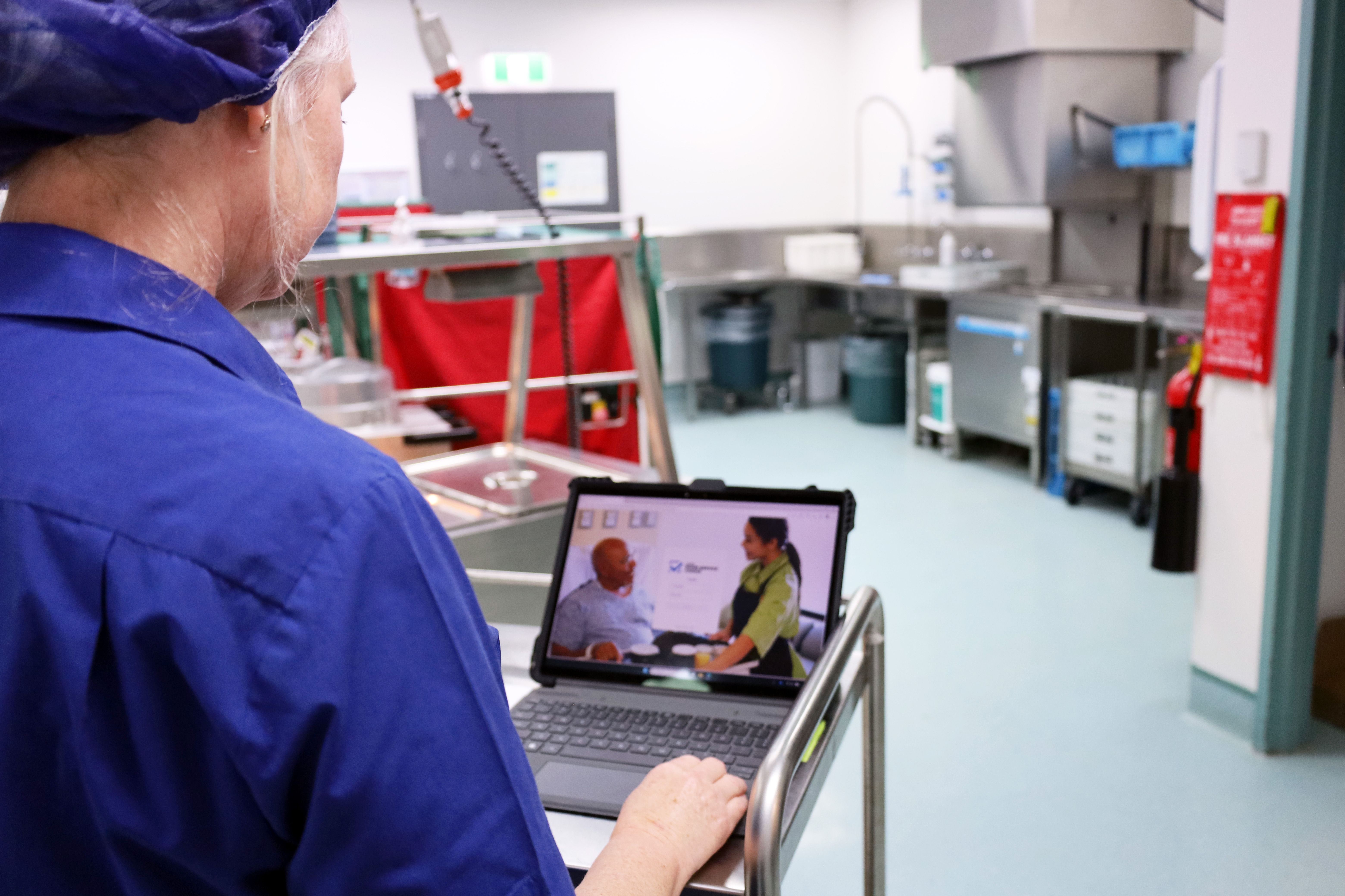 side profile of food service worker, using a laptop. The laptop shows an image of a man and woman having a discussion