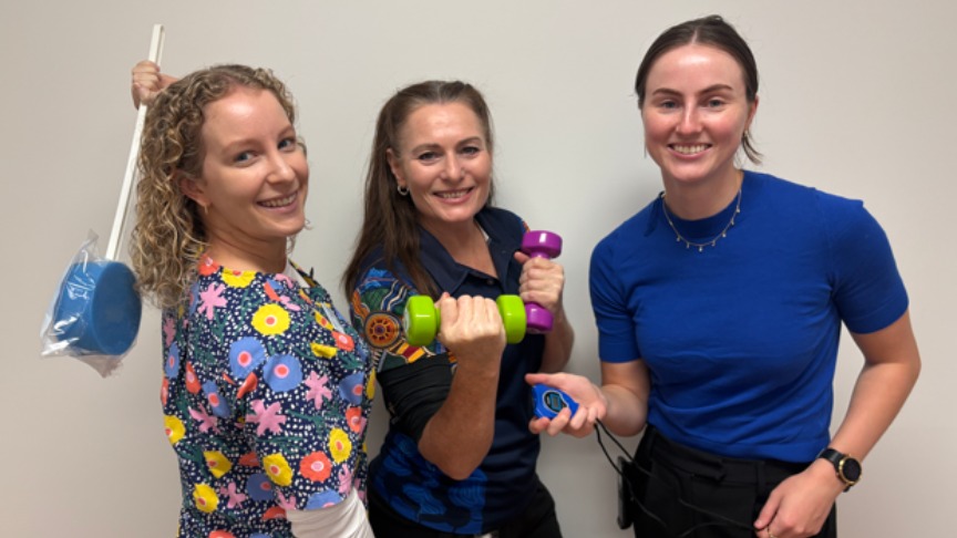 Three women in matching blue shirts are exercising with dumbbells and a blue sponge, promoting health and fitness.
