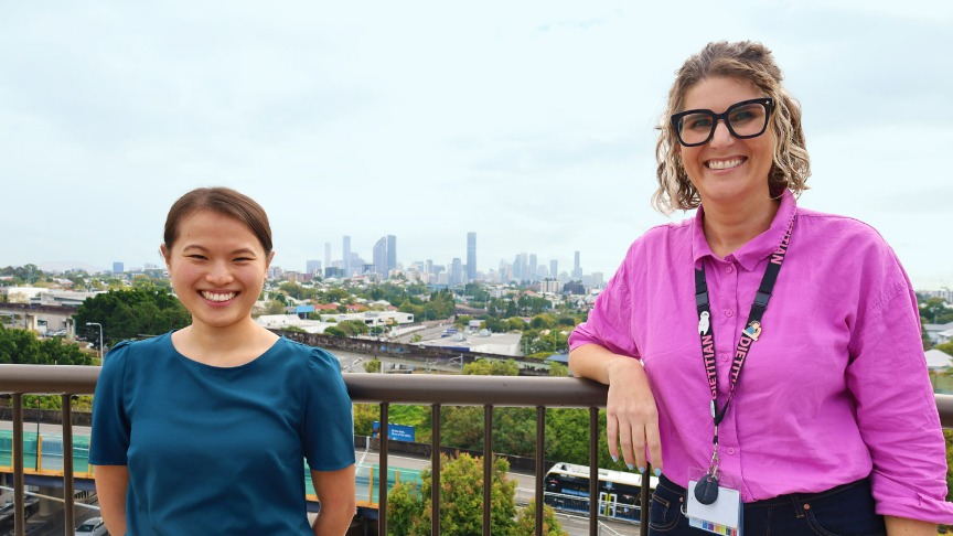 Two women leaning on a balcony rail with Brisbane City in the background
