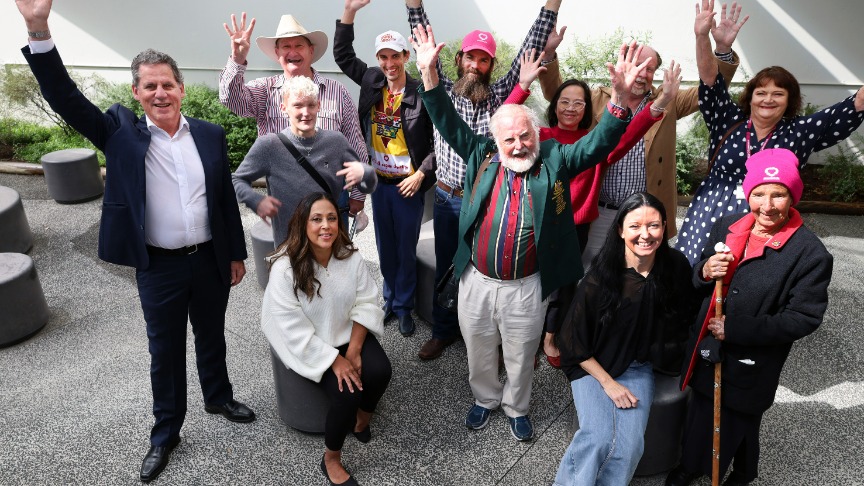 A joyful group of liver transplant recipients at their 40-year celebration, standing together with hands uplifted