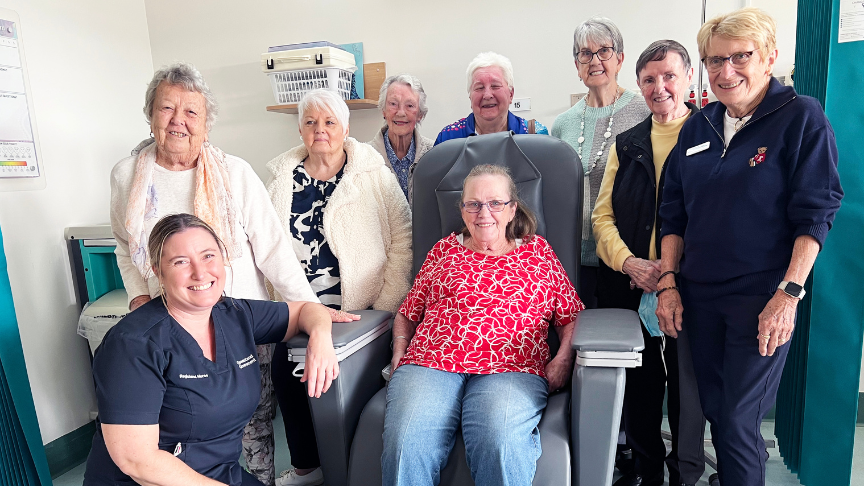 Large group of women standing (one sitting) in front of a new infusion chair