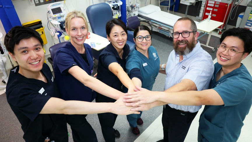 A group of six multidisciplinary clinicians including three men and three women from multiple cultures who provide Radiation Oncology care to patients doing the teamwork hand stack gesture
