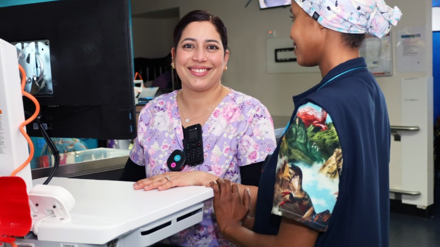 A Clinical Facilitator in bright scrubs teaches a staff member in a hospital room, focusing on patient care and nursing practices