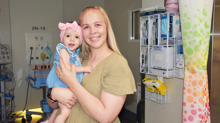 Woman holding a baby girl in from of a neonatal bed
