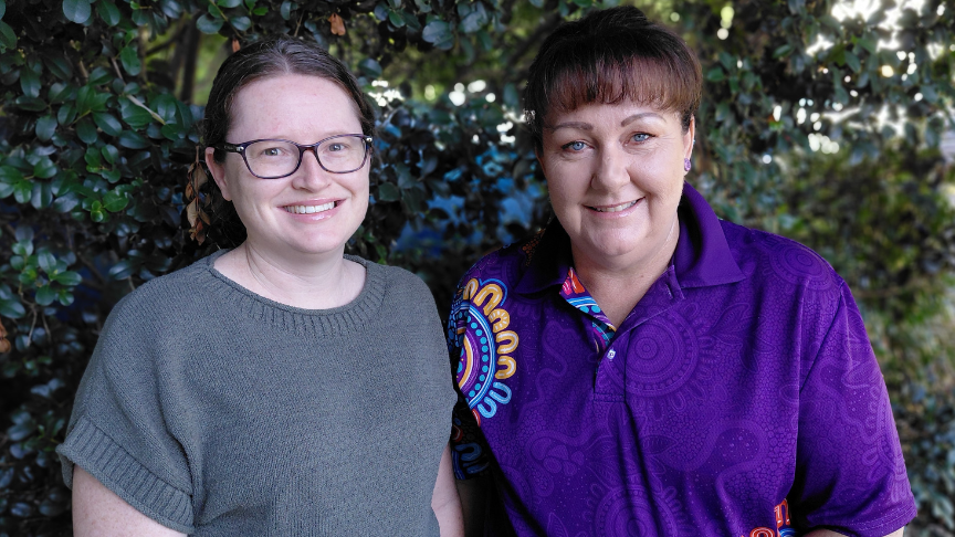 two women standing in front of greenery