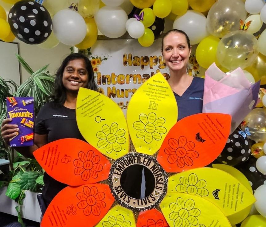Two nurses holding up a paper sunflower