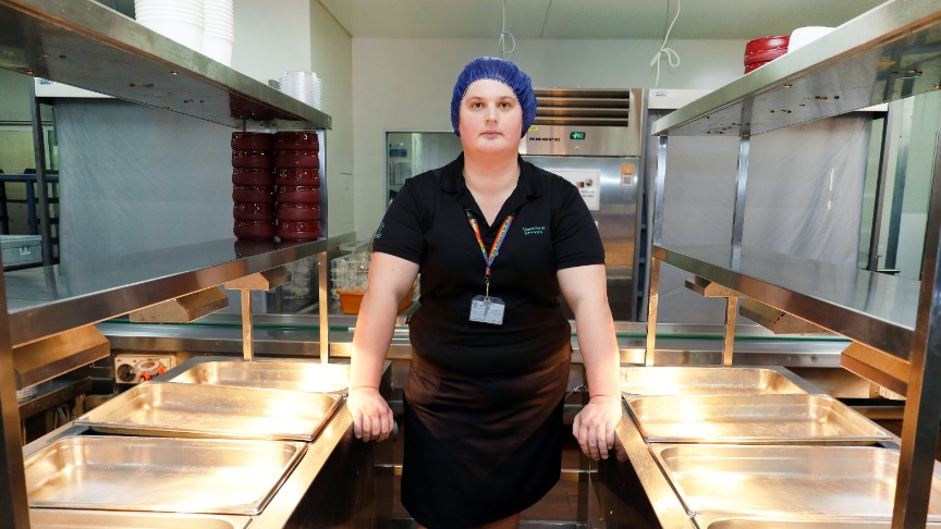 Female Food Services worker standing between two bain-maries.