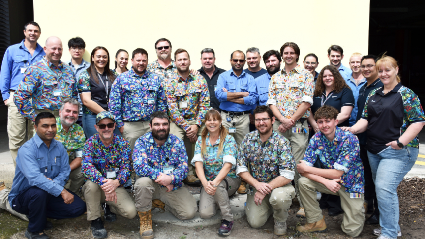A large group of building and maintenance workers posing in front of a yellow wall