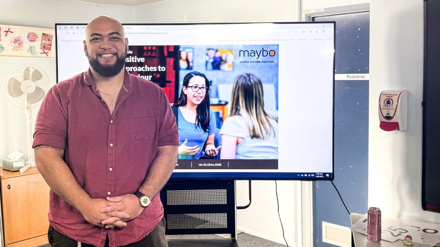Workplace Aggression Trainer Jacob Tua stands in front of a screen displaying a training powerpoint 