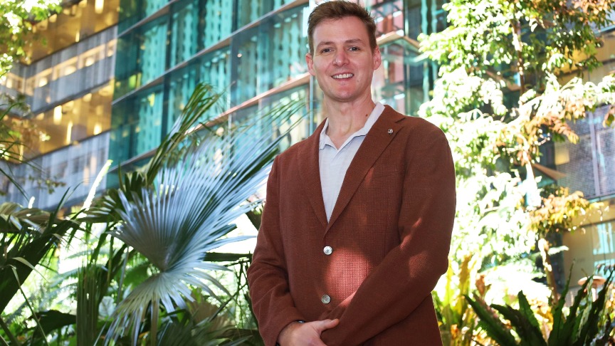 Mike Trott in a suit stands confidently in front of a green building, showcasing a professional appearance