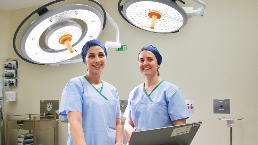 Two healtcare workers wearing scrubs standing in theatre