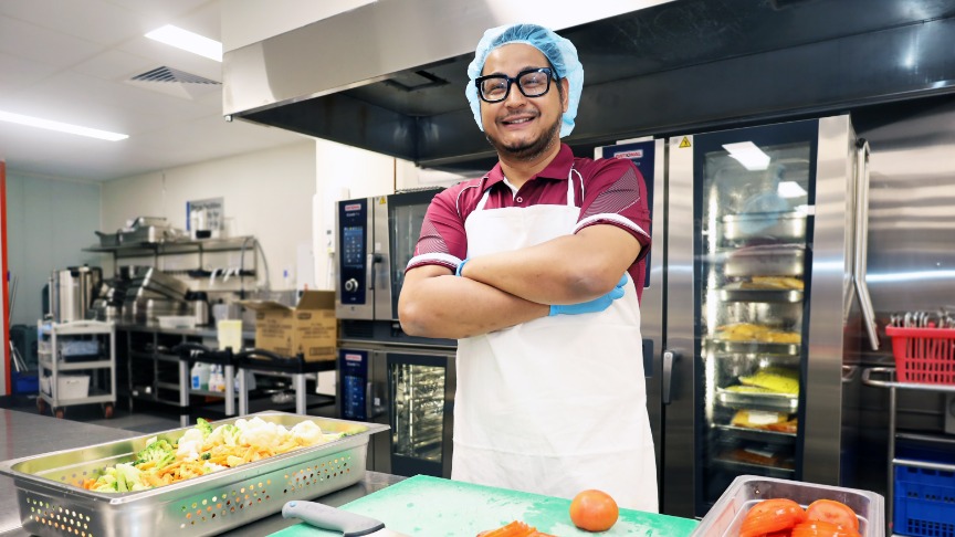 Man standing in hospital industrial kitchen smiling with arms crossed.