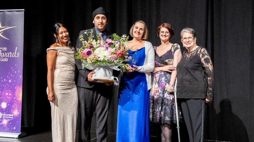 A small group of people wearing formal clothes, two holding a large bunch of flowers