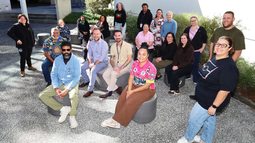 Group of First Nations staff scattered in hospital courtyard, smiling at camera.