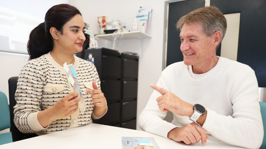 action shot of female speech pathologist and male patient pointing at a flash card