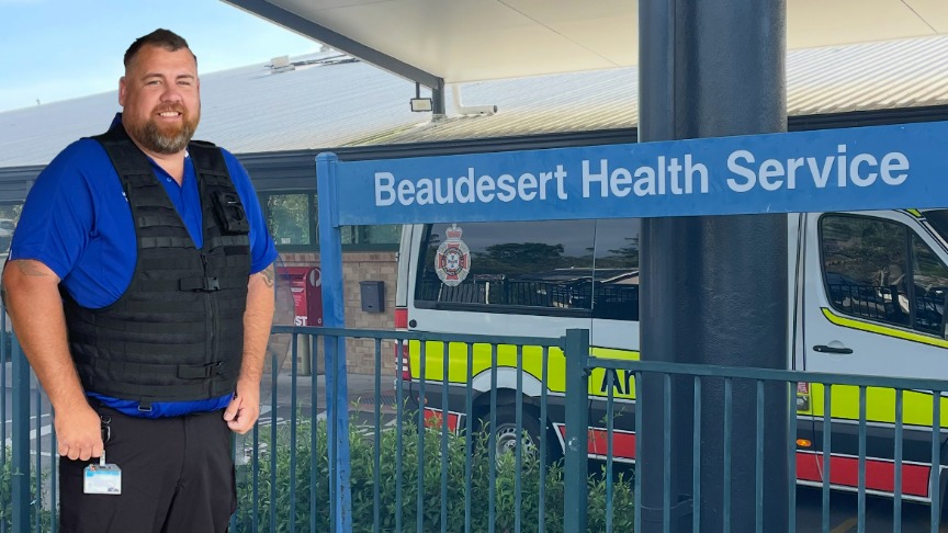 Man in a blue tshirt standing in front of a Beaudesert Hospital sign