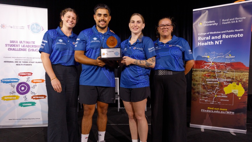 Indigenous allied health students hold trophy on stage.
