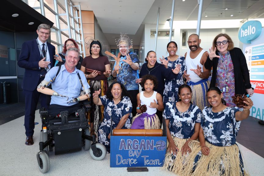 A group of men and women representing different cultures with traditional dress pose with excitement in a hospital foyer
