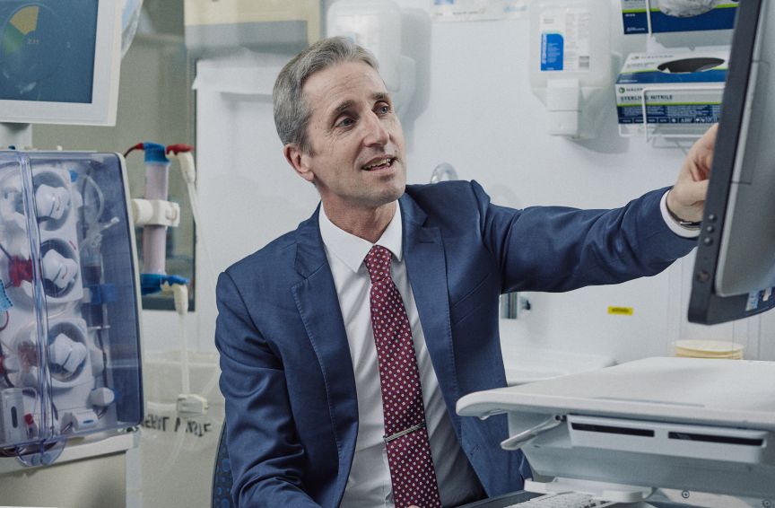 A senior male doctor operates a computer at the bedside near a dialysis machine