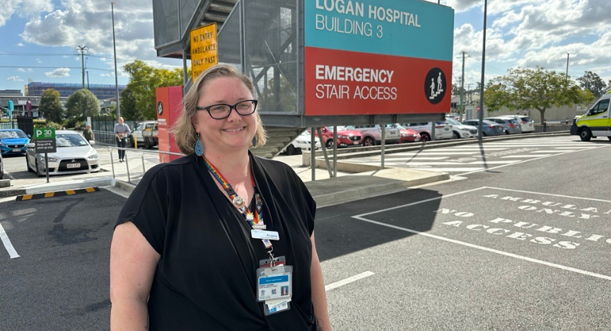 A person stands in front of Logan Hospital Building 3, near the Emergency Stair Access sign, wearing a staff badge and lanyard.
