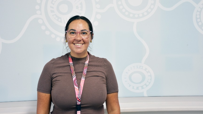 Woman wearing brown shirt and glasses standing in front of frosted glass with indigenous decal