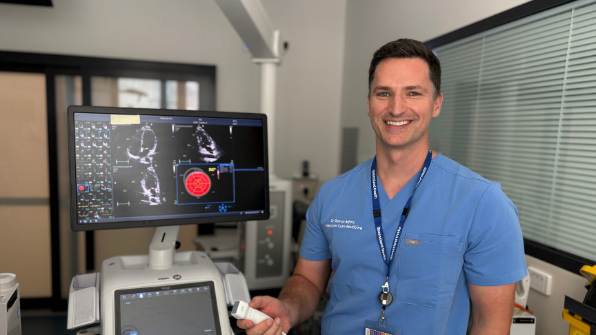 Male doctor smiling next to echocardiogram