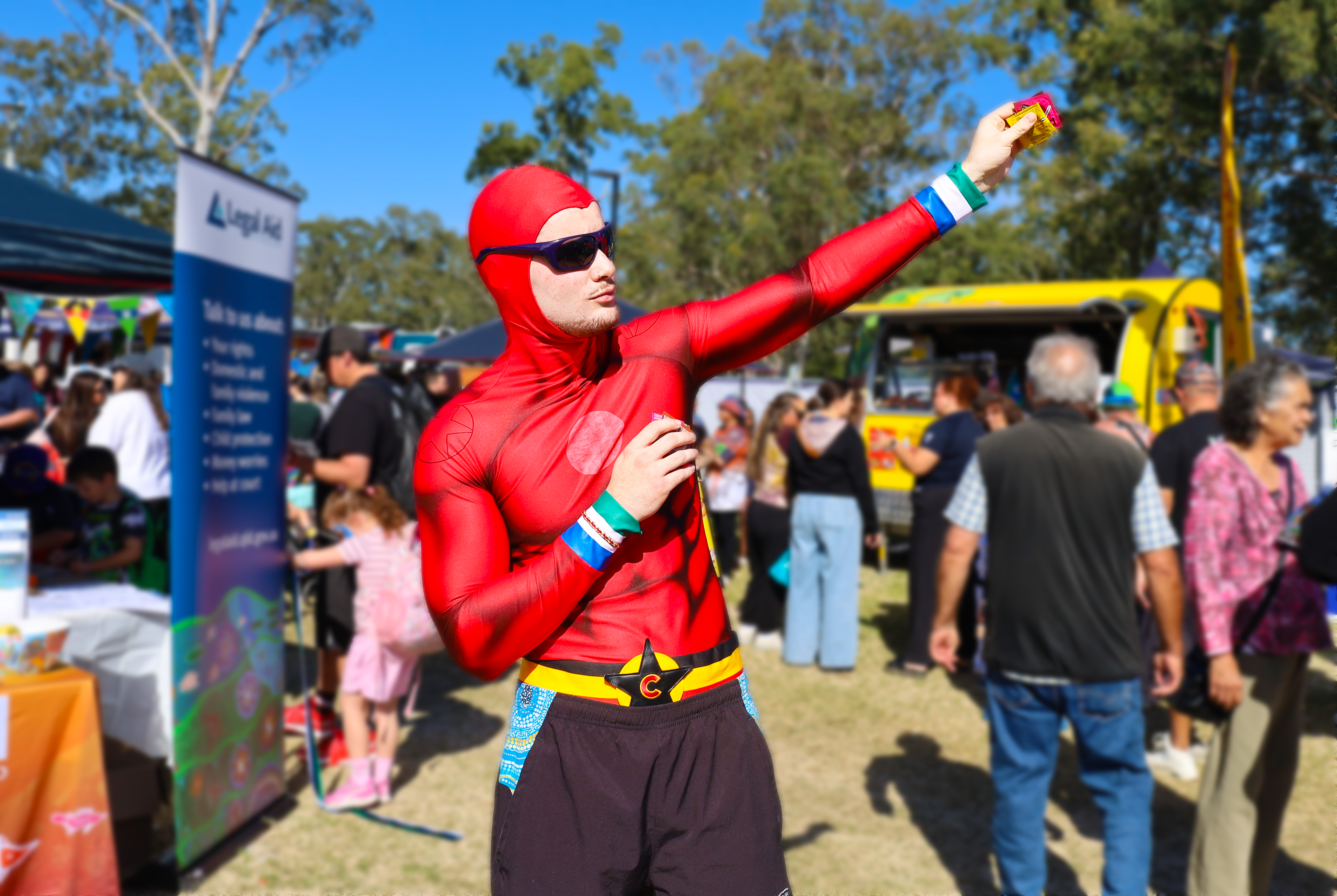 A superhero (Condoman) wearing a red suit and shorts holds a strong pose with his arm outstreched holding condom packets.
