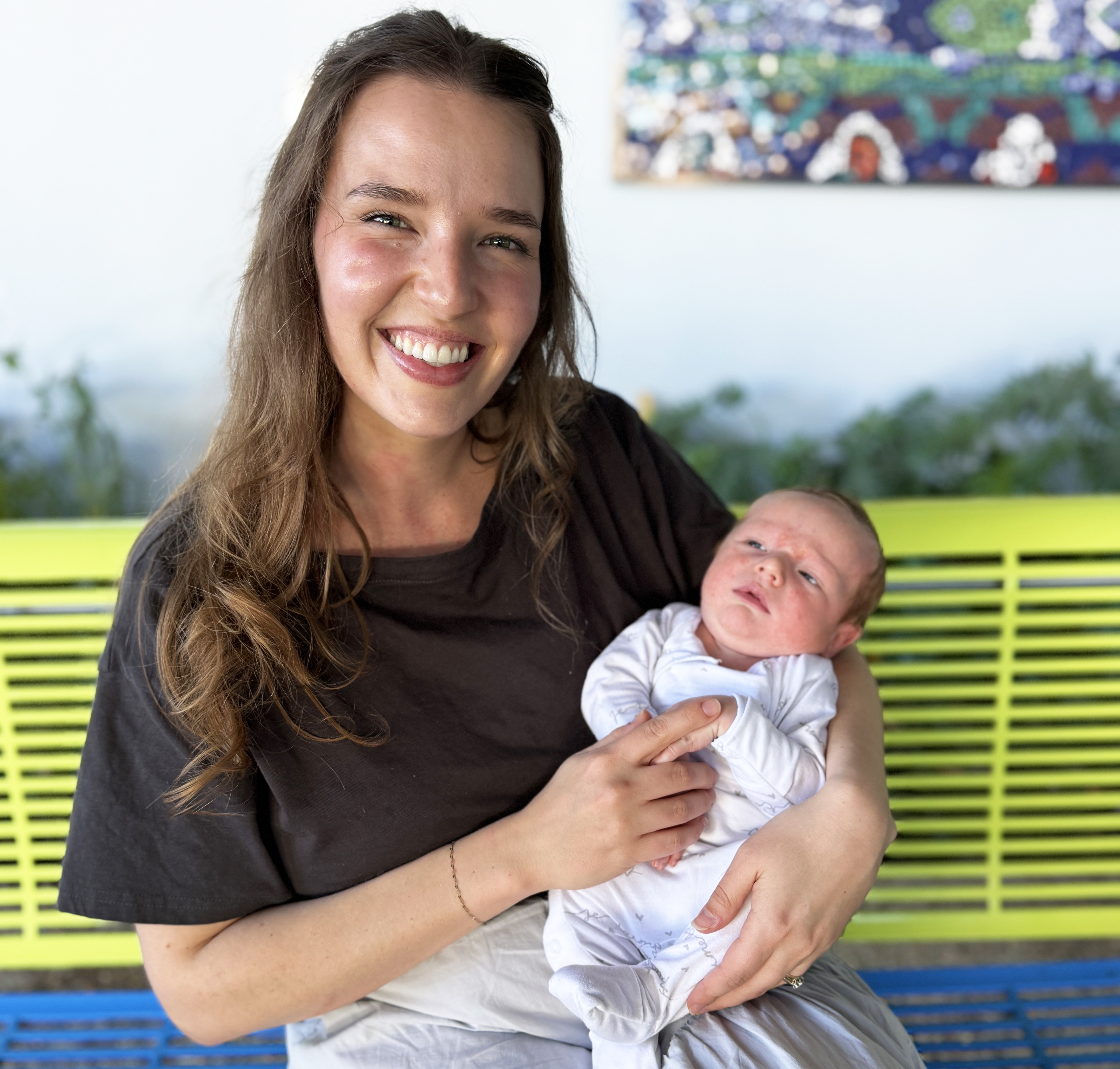 Young mother holding newborn baby, sitting on a yellow chair
