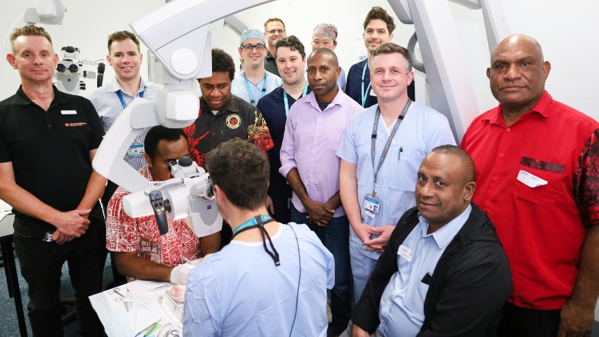 A group of surgeons from Australia and Papua New Guinea in a clinical setting with a surgical robot