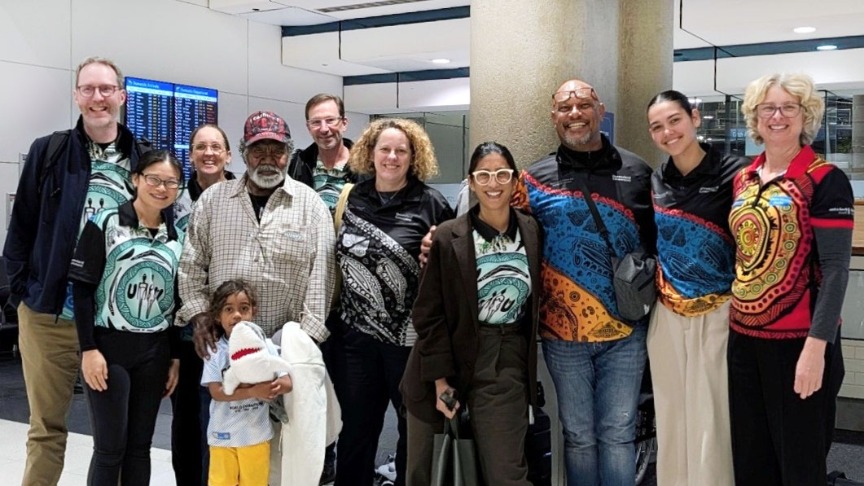 A group of transplant staff and Uncle Mervyn posing together at the airport, smiling for the camera