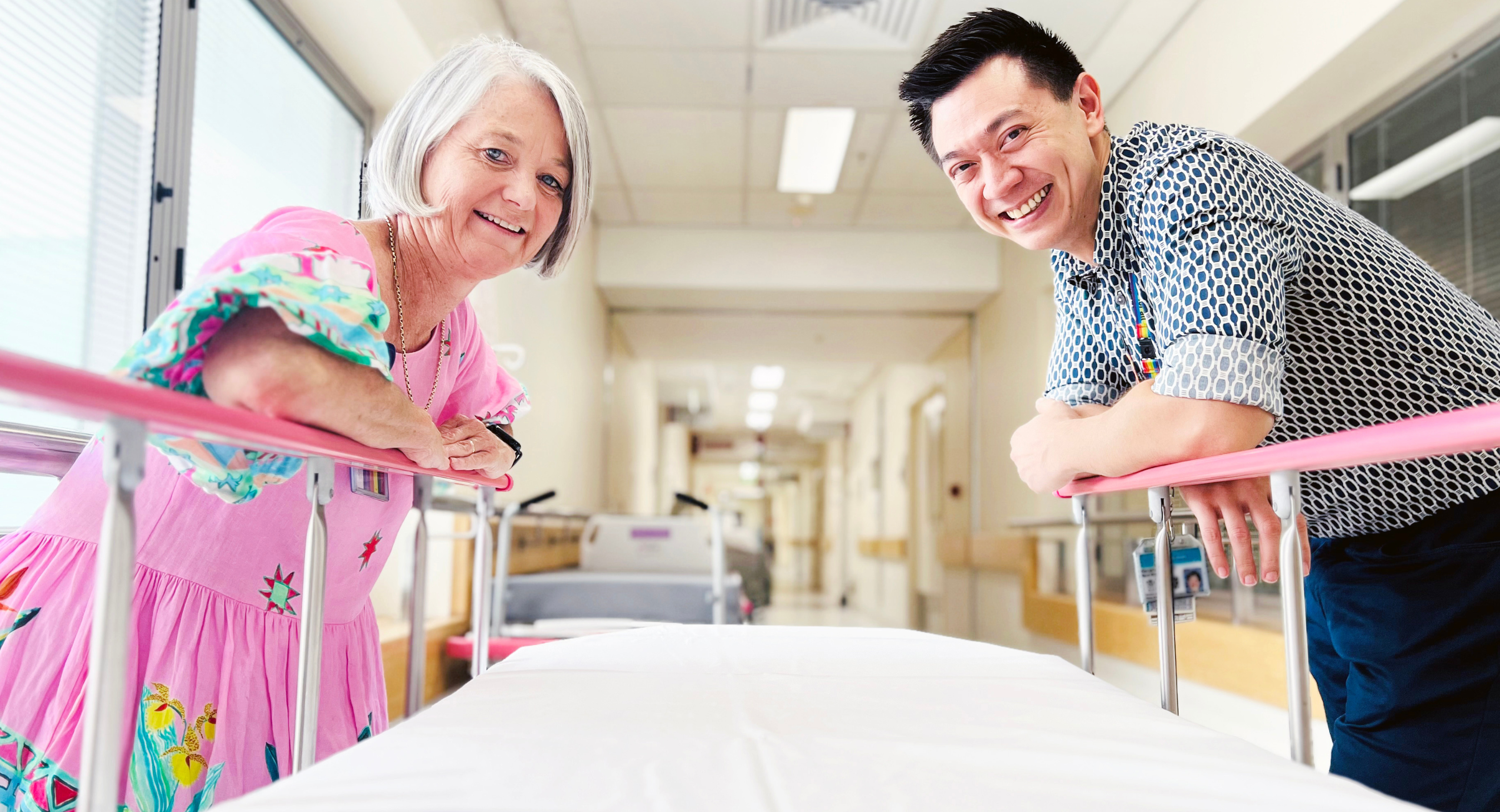 Two clinicians leaning over opposite sides of a hospital bed smiling