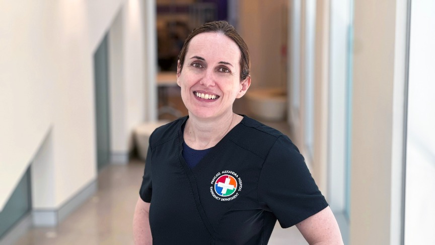 A female doctor wearing black branded scrubs smiling in a corridor 