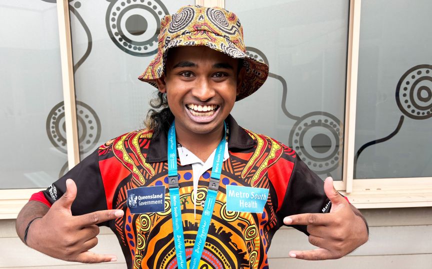 Peer worker Ari is dressed in a hat and a shirt featuring a vibrant tribal design, reflecting his cultural identity