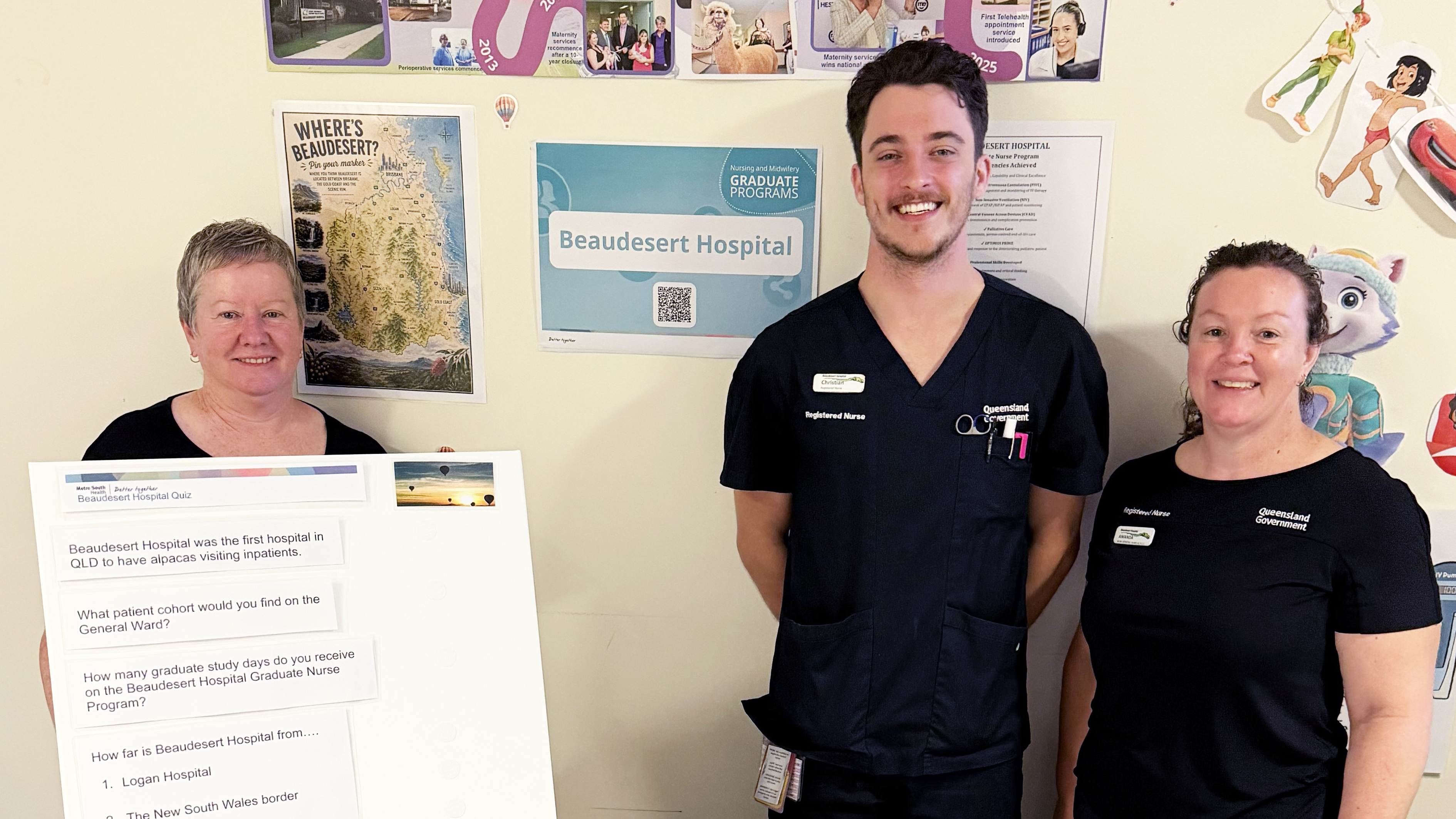 Three nurses in navy scrubs standing with a table at an info stall