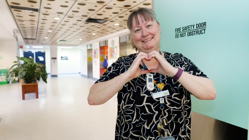 Woman making heart hands in a hospital corridor