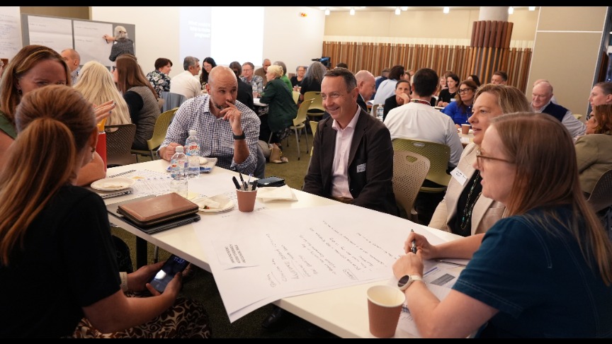 candid shot of people gathered at tables and talking in conference room