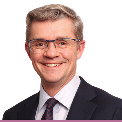 A person with short light brown hair wearing glasses, a pin striped suit, white shirt and tie.